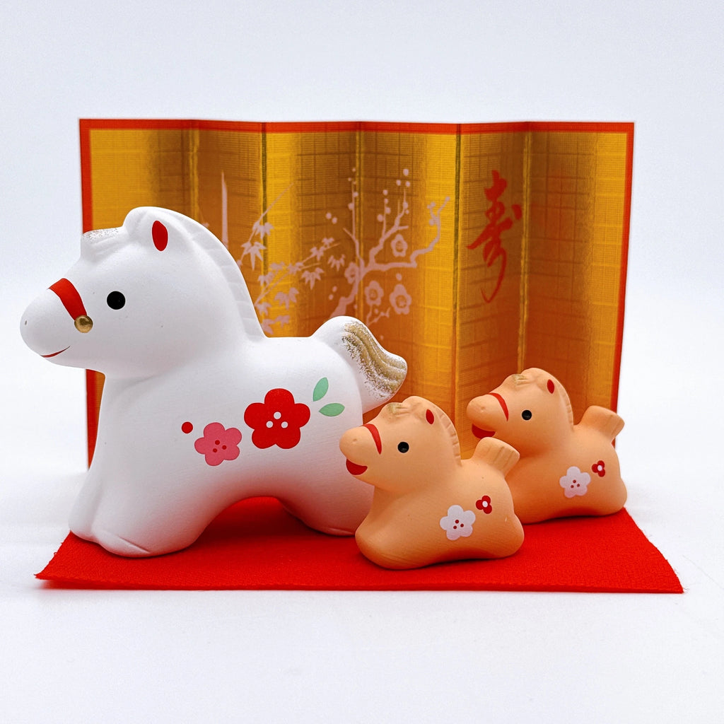 Decorative horse figurine with two smaller horses on a red mat against a yellow background