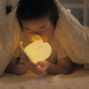 Twinkle Glory silicone cuckoo night light glowing with warm yellow light held by a child under a cozy blanket