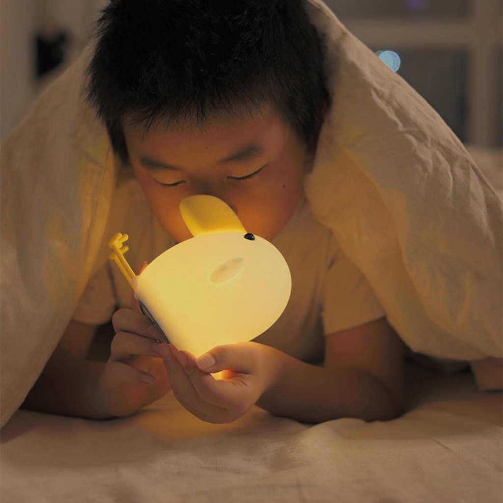 Twinkle Glory silicone cuckoo night light glowing with warm yellow light held by a child under a cozy blanket