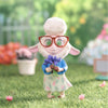 Toy figure of a character with glasses holding flowers in a garden setting