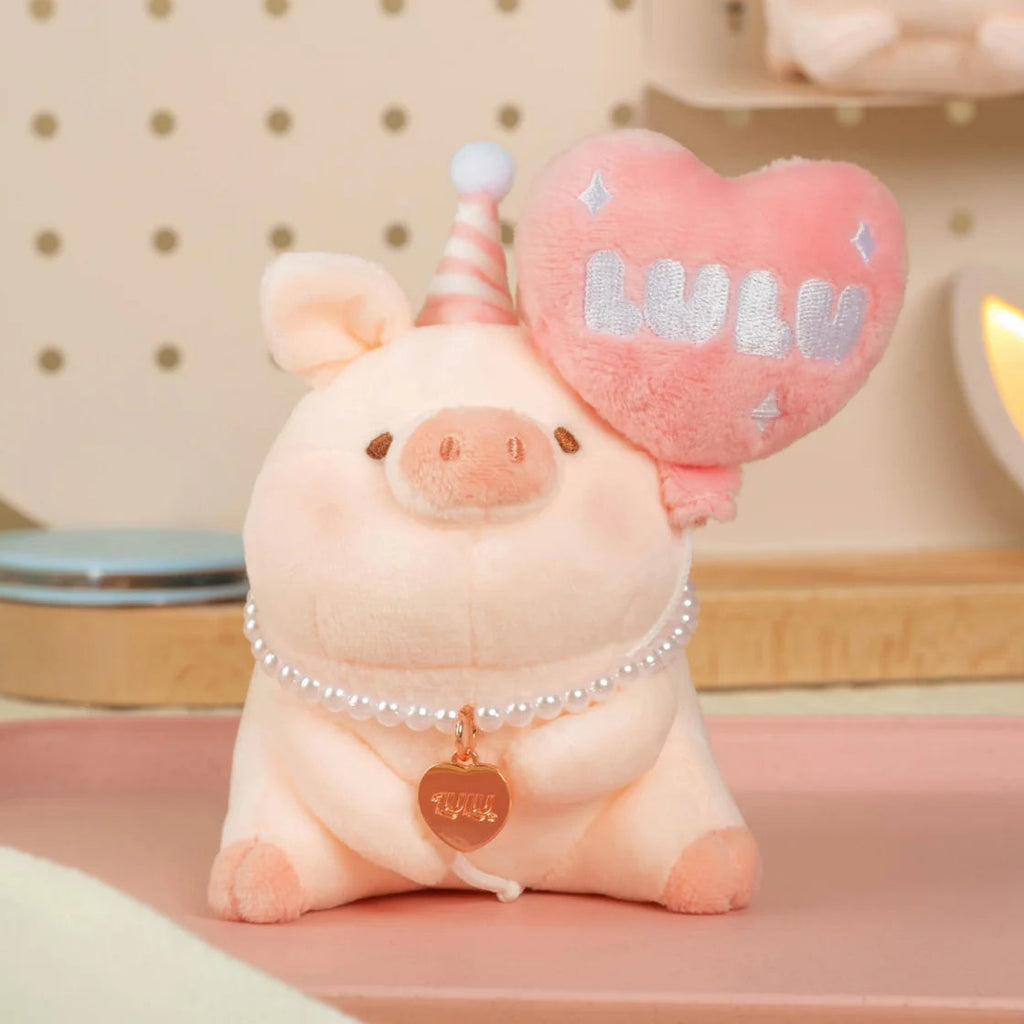 Plush pig toy with a heart-shaped pillow labeled 'LOVE' on a pink surface.