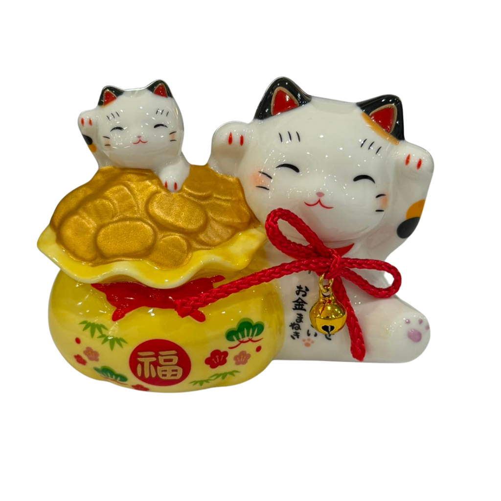 A Japanese maneki-neko lucky cat figurine with a white body, black ears, red accents, and a gold ingot resting on its head, tied with a red cord and bow, with a small gold bell hanging from its neck. The figurine is set against a plain white background.