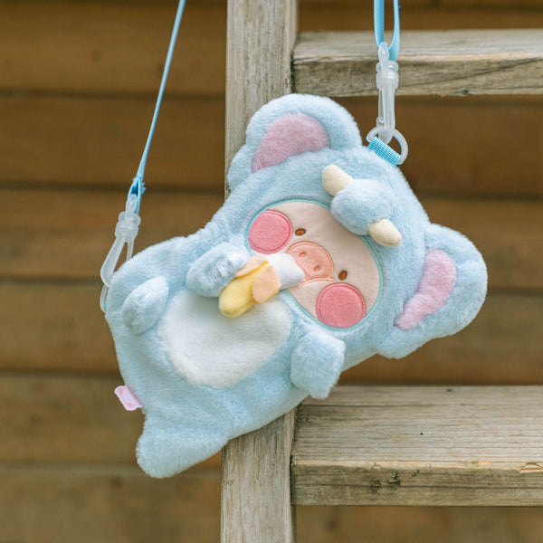 Plush toy with a blue outfit and pink accents hanging on a wooden surface.