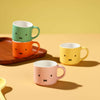 Four colorful mugs with facial expressions on a yellow background