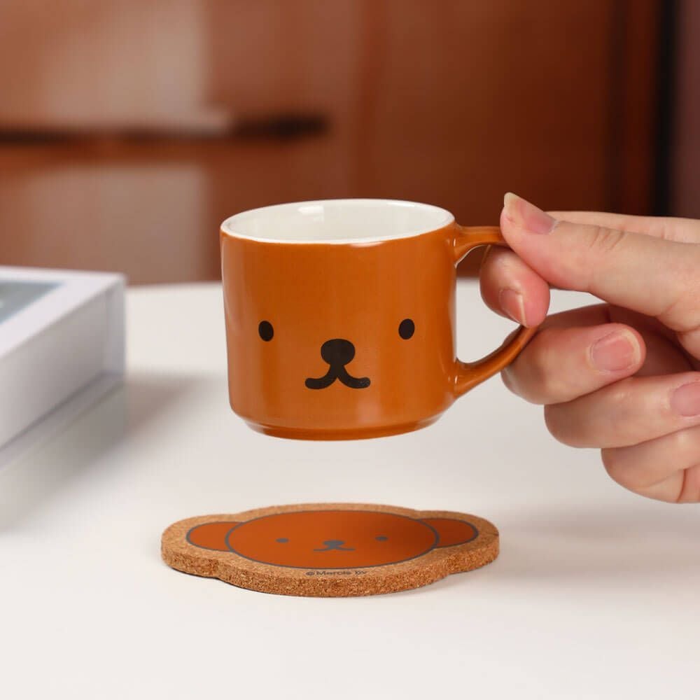 Person holding a brown mug with a bear face design on a white surface.