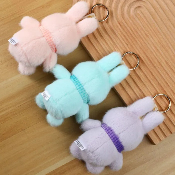 Three plush keychains shaped like dogs in pink, green, and purple on a wooden surface.