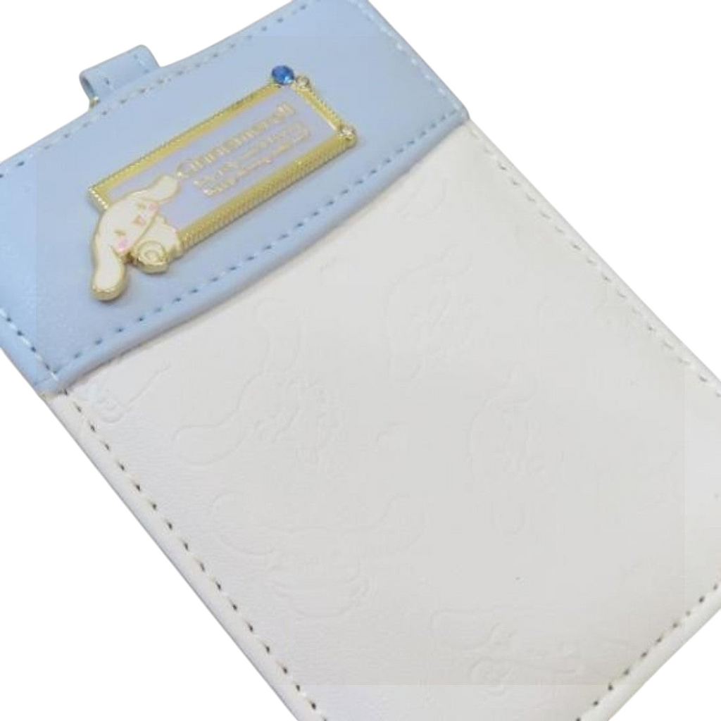 A Sanrio Cinnamoroll-themed card holder or ID badge sleeve featuring a light blue leatherette flap with a gold-tone metal plaque and a small Cinnamoroll charm, paired with a white embossed body.
