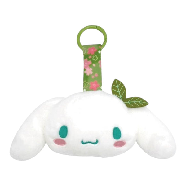 A white plush character accessory with long floppy ears, embroidered teal eyes and mouth, pink cheeks, and a green floral hanging strap with two green leaves, shown on a plain white background.