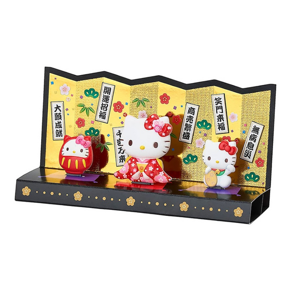 A decorative Hello Kitty display set on a black base with a gold folding screen backdrop. The set includes a white Hello Kitty figure in a red kimono, a red Daruma doll, and smaller red-and-white Hello Kitty figures, with Japanese text panels and floral details.