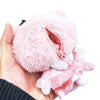 A small pink plush character coin purse held in a hand, featuring a fuzzy body, a zippered opening, and a satin dress detail on a plain white background.