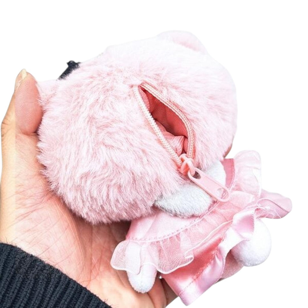 A small pink plush character coin purse held in a hand, featuring a fuzzy body, a zippered opening, and a satin dress detail on a plain white background.