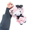 A hand wearing a dark gray knit sweater holds a pink plush doll keychain with black bows and lace details against a plain white background.