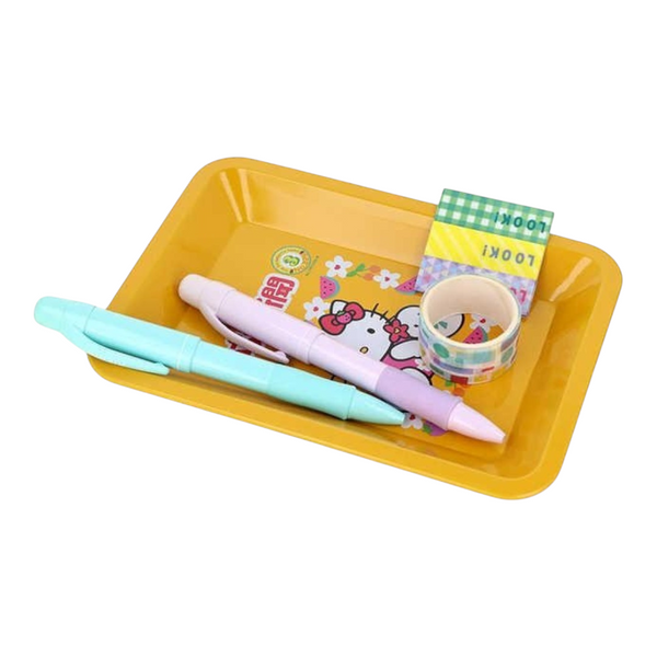 A yellow Metal tray holding two pastel pens, a small roll of patterned washi tape, and a Hello Kitty card on a white background.