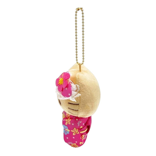 A small plush keychain charm shaped like a stylized face in a cream-colored head and bright pink floral clothing, hanging from a gold ball chain on a plain white background.