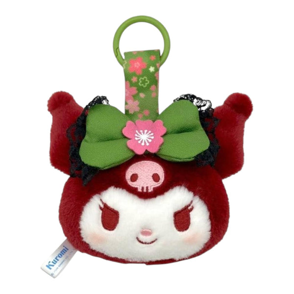 A Sanrio Kuromi plush keychain or bag charm, featuring a round red and white character head with a green bow, pink flower, and black lace trim, complete with a green carrying ring at the top.