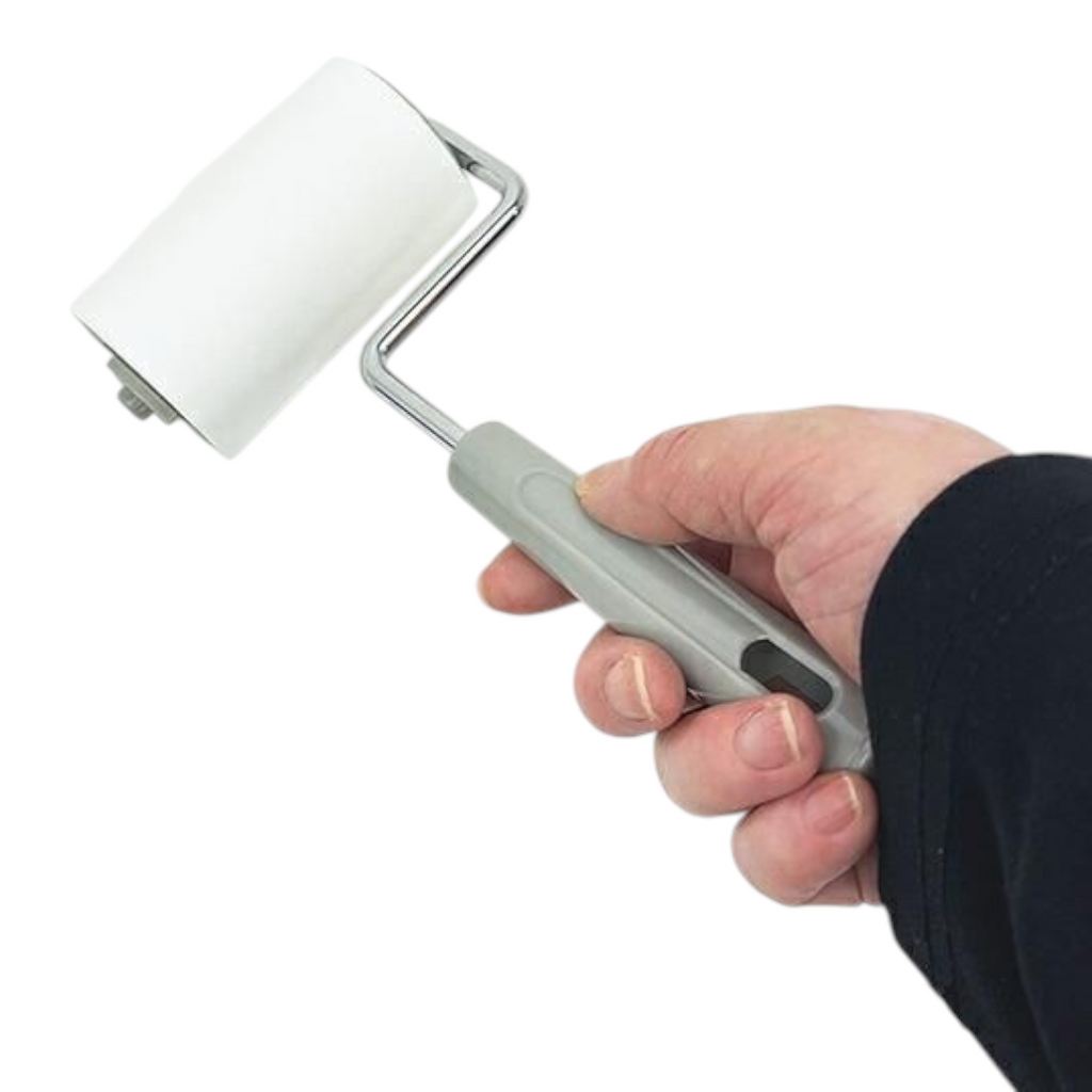 A hand holding a small paint roller with a white foam roller surface, a gray handle, and a silver metal frame against a plain white background.