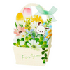 A decorative gift basket card or box featuring layered floral illustrations, including tulips, daisies, and small green leaves, with a cartoon sheep face and a mint green ribbon bow on a white background.