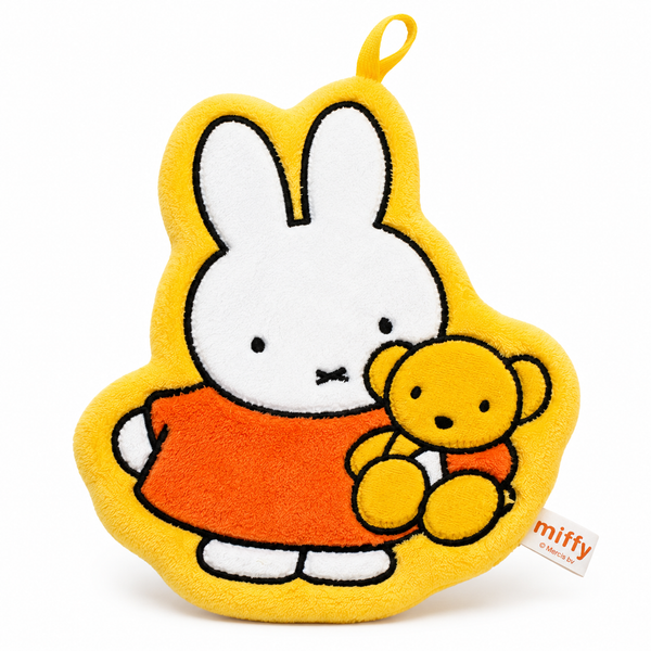 A plush Miffy character hand towel in yellow, white, and orange, holding a small yellow teddy bear, photographed on a clean white background. A small 'miffy' brand tag is visible on the lower right.