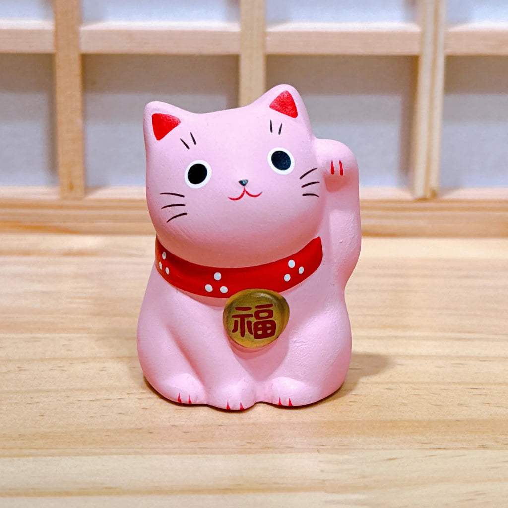 Pink cat-shaped figurine with a red collar on a wooden surface