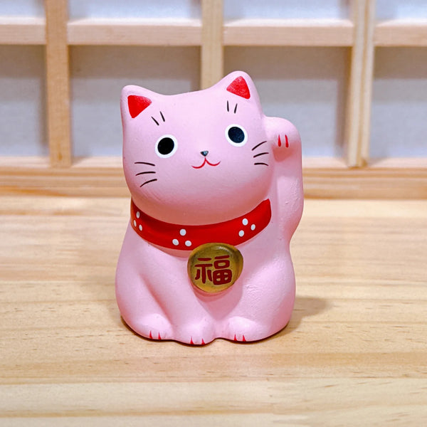 Pink cat-shaped figurine with a red collar on a wooden surface