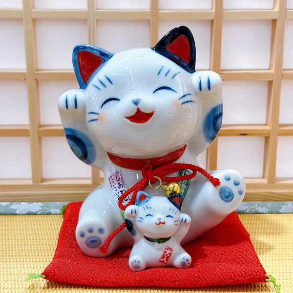 White cat figurine with blue accents and red string on a red cushion against a wooden panel background.