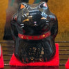 Twinkle Glory black Japanese Maneki Neko figurine with gold calligraphy and red collar on a small red felt mat