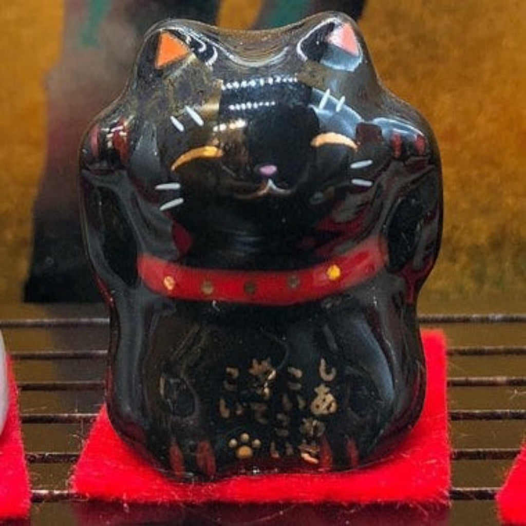 Twinkle Glory black Japanese Maneki Neko figurine with gold calligraphy and red collar on a small red felt mat