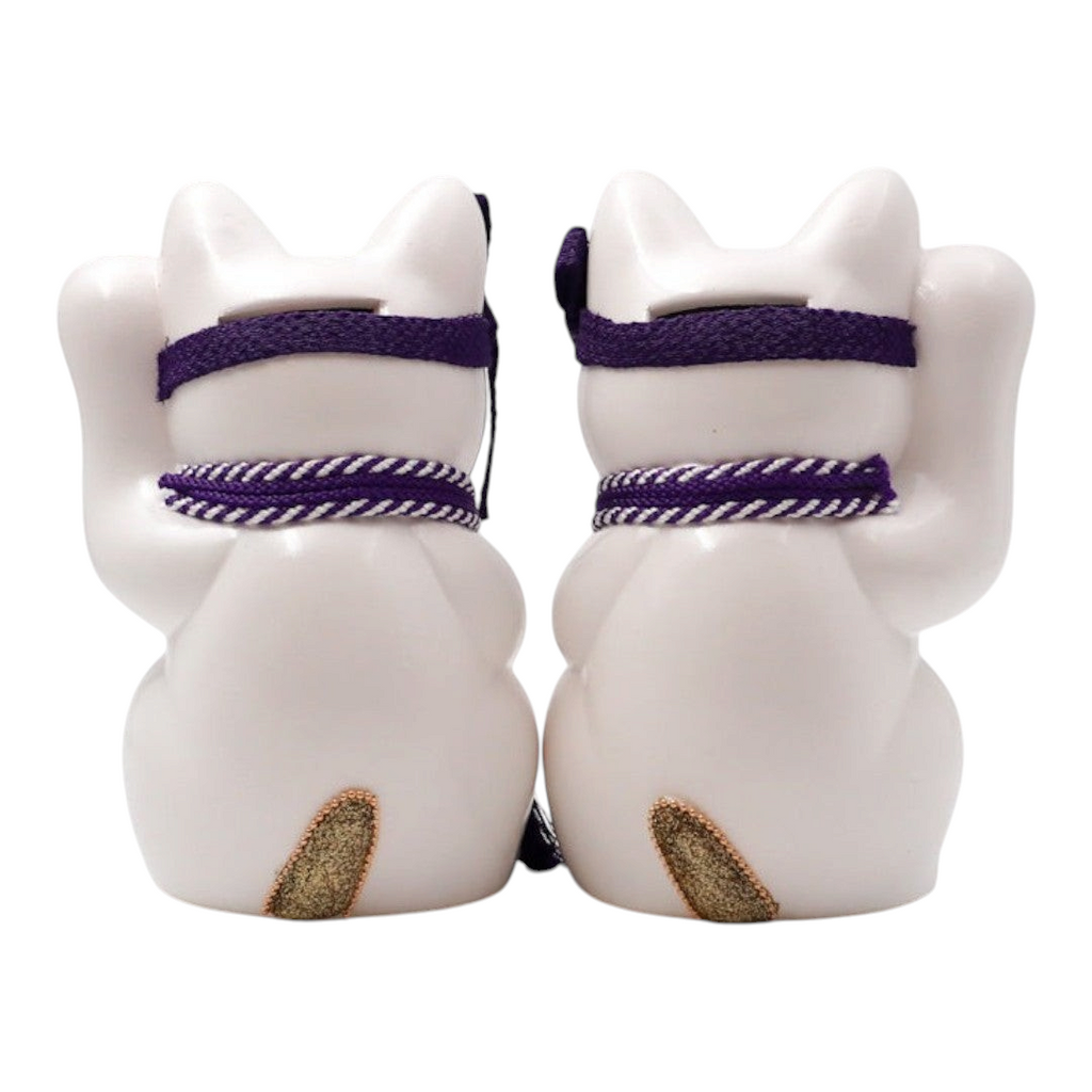 Back view of two Twinkle Glory Goenneko ceramic lucky cats with purple headbands and gold tails on a white background