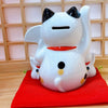 Twinkle Glory white ceramic Maneki Neko lucky cat piggy bank with black ears and red collar on a red cushion
