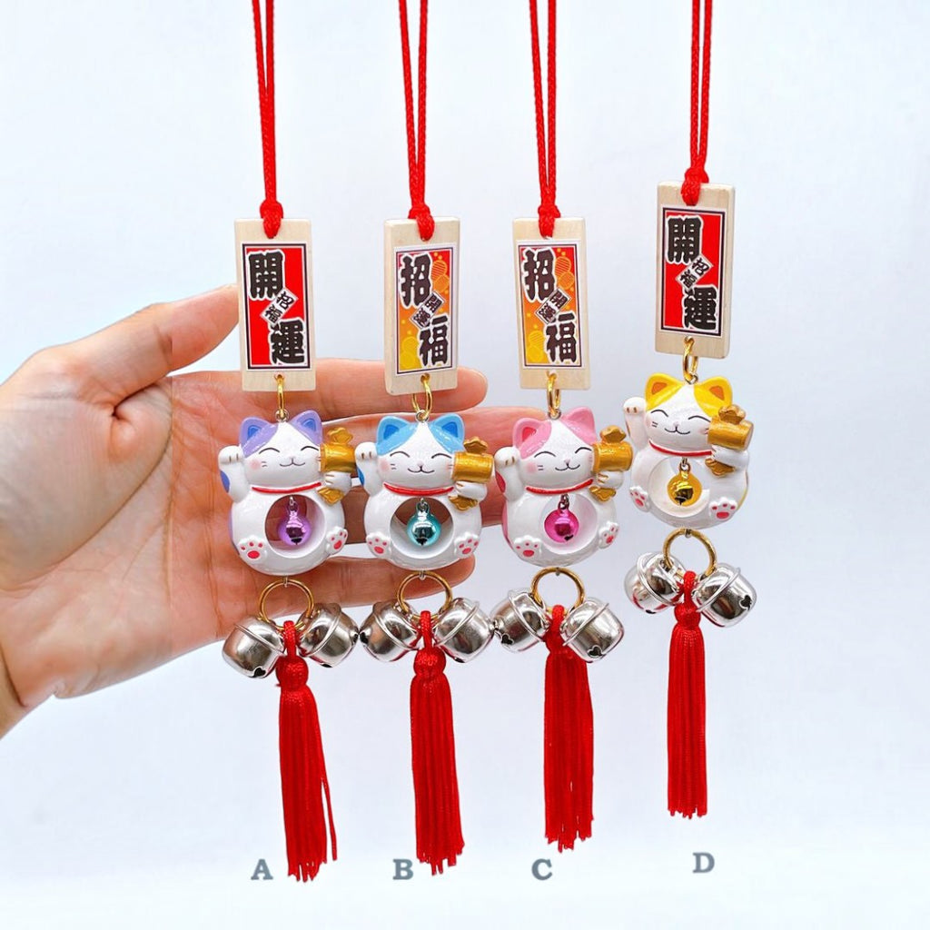 Twinkle Glory Japanese lucky cat charms in purple, blue, pink, and yellow with red tassels and hanging bells.