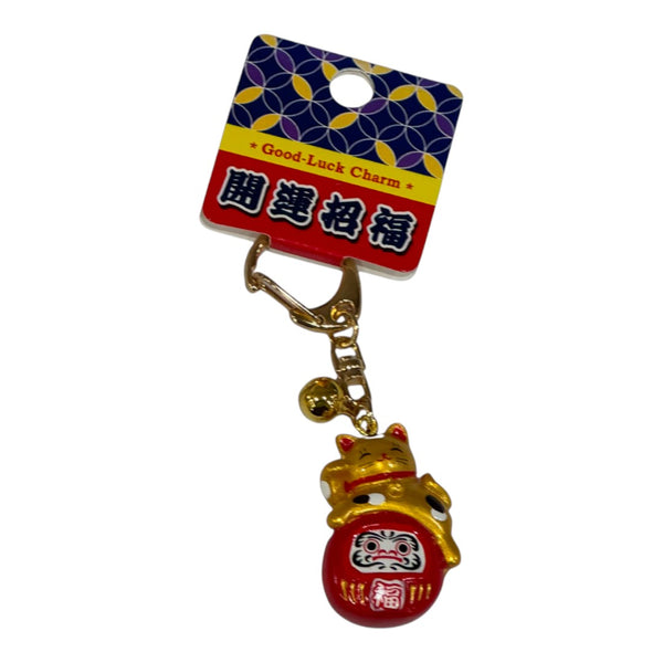Twinkle Glory gold Maneki-Neko lucky cat and red Daruma doll charm keyring on a Japanese good luck display card