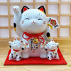 Twinkle Glory ceramic Maneki Neko lucky cat piggy bank with two smaller cat figurines on a red fabric mat