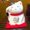 Twinkle Glory Japanese Maneki Neko lucky cat figurine with white ceramic, black spots, and red collar on a red mat