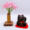 Twinkle Glory Yakushigama mini black lucky cat figurine on a red mat with a small pink flower arrangement