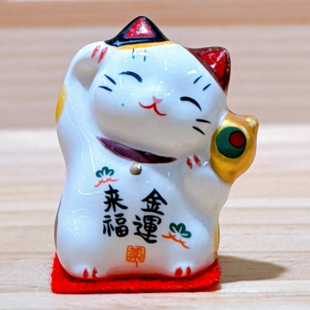 Twinkle Glory Yakushigama mini ceramic lucky cat figurine with a smiling face and gold coin on a red felt base.