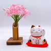 Twinkle Glory Yakushigama mini lucky cat figurine on a red mat next to a small bamboo vase with pink flowers