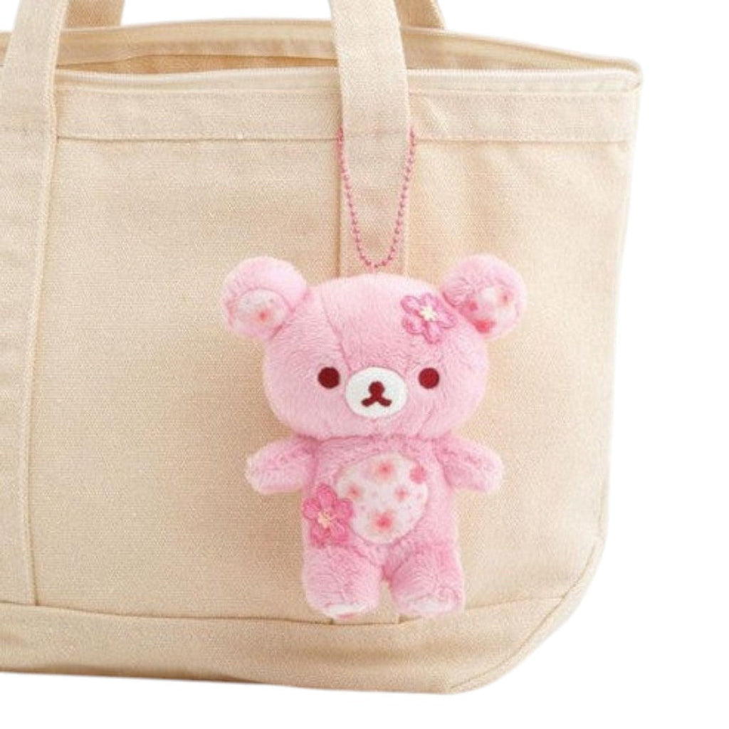 Twinkle Glory San-X Rilakkuma cherry blossom plush keychain in soft pink polyester hanging on a beige canvas tote bag