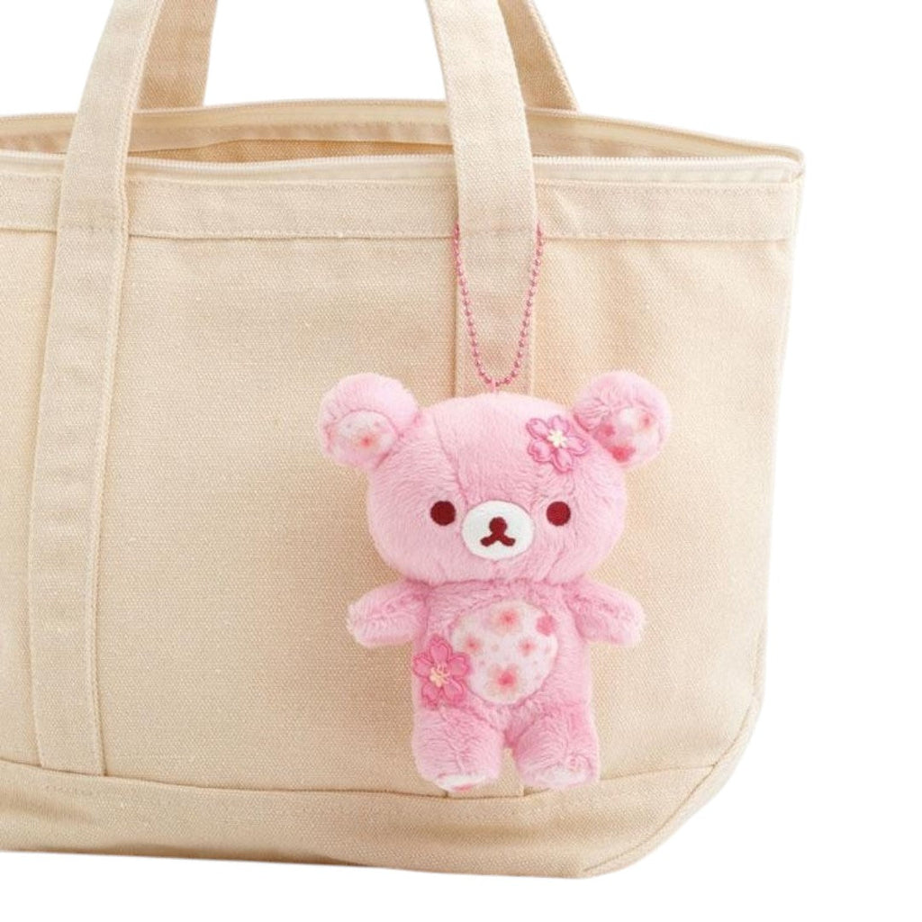 Twinkle Glory San-X Rilakkuma plush keychain in cherry blossom pink with sakura flower details attached to a tote bag