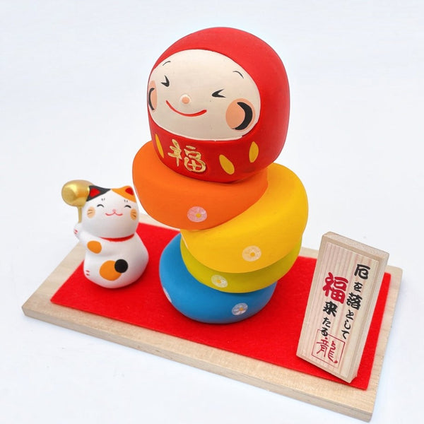 Twinkle Glory Ryukodo porcelain lucky cat and colorful Daruma Otoshi stacking game set on a red cloth and wooden base