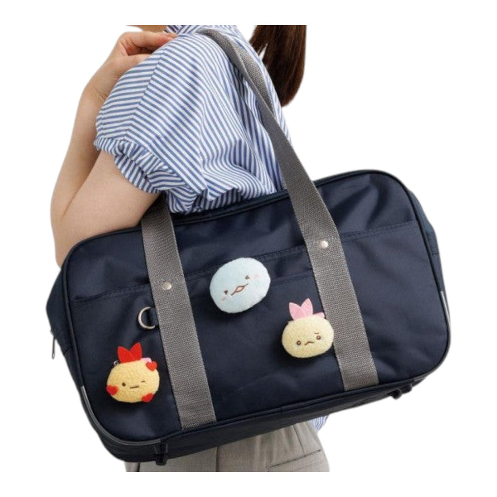 Twinkle Glory San-X Sumikko Gurashi plush badges attached to a navy blue school bag worn on a person's shoulder