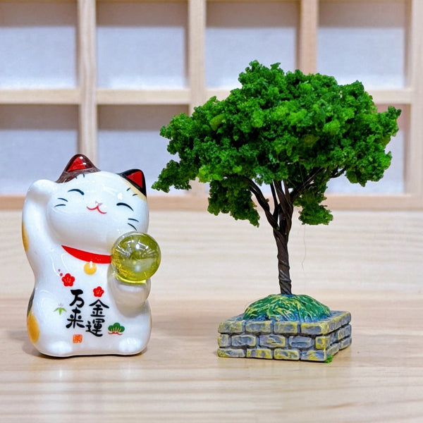 Twinkle Glory Yakushigama porcelain lucky cat figurine holding a golden orb next to a miniature green tree model