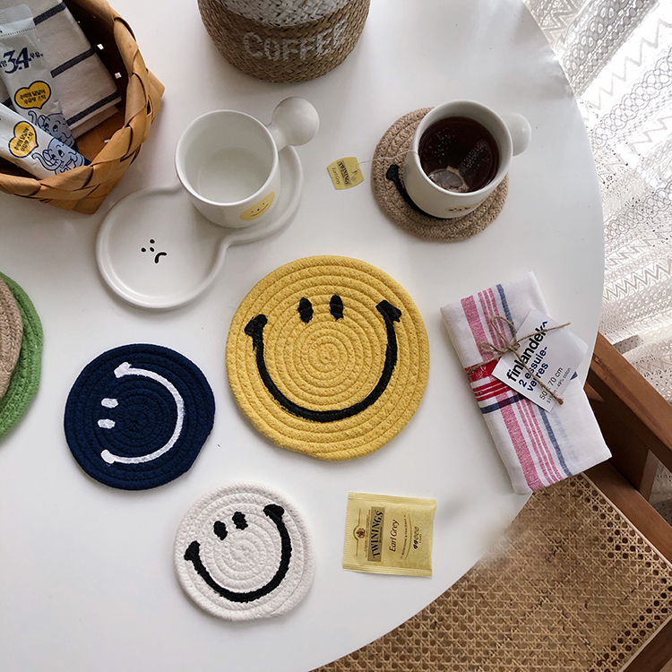Cup of coffee on a brown Smiley Face coaster next to blue, yellow and white Smiley Face mat coasters 