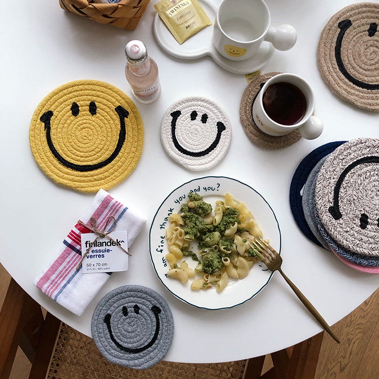 A variety of different coloured Smiley Face mat coasters adjacent to a mug using a brown Smiley Face coaster